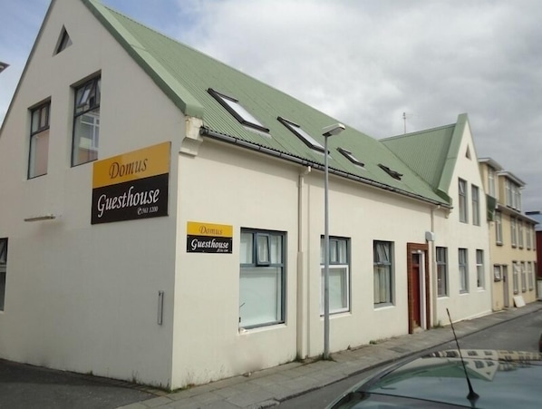 A building with a sign reading "Domus Guesthouse" and a contact number.