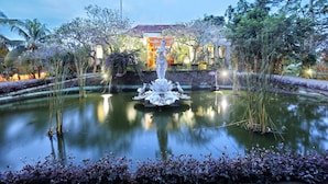 A serene garden with a central fountain, surrounded by lush greenery and a building in the background. - Bhanuswari Resort & Spa (Ubud)