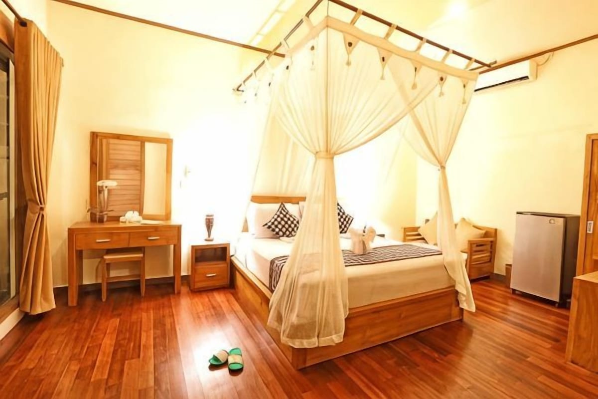 A bedroom with a four-poster bed, a desk, a chair, a wardrobe, and a bedside table.
