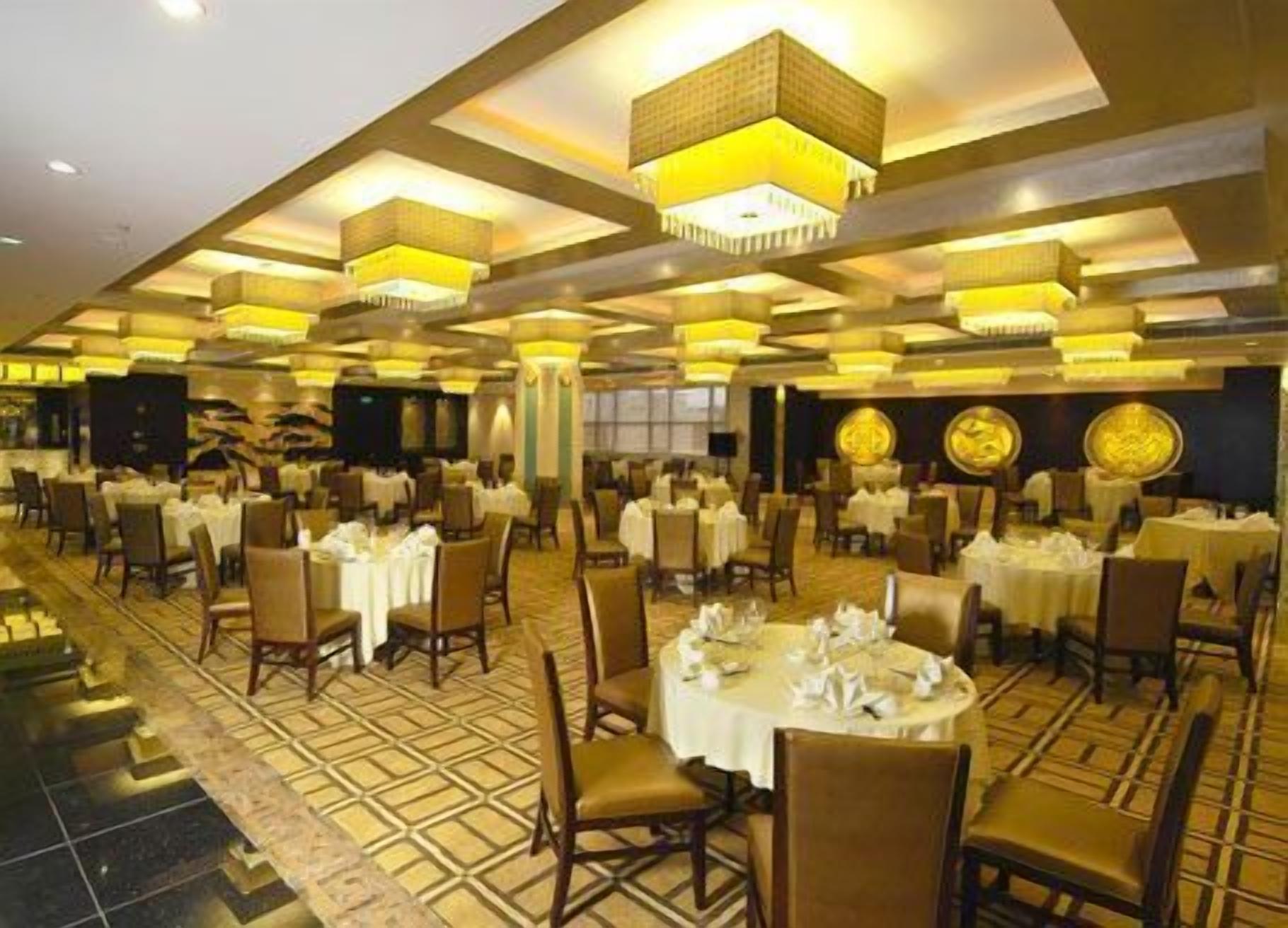 Une vaste salle de banquet dotée de nombreuses tables rondes, chacune recouverte d’une nappe blanche et entourée de chaises.