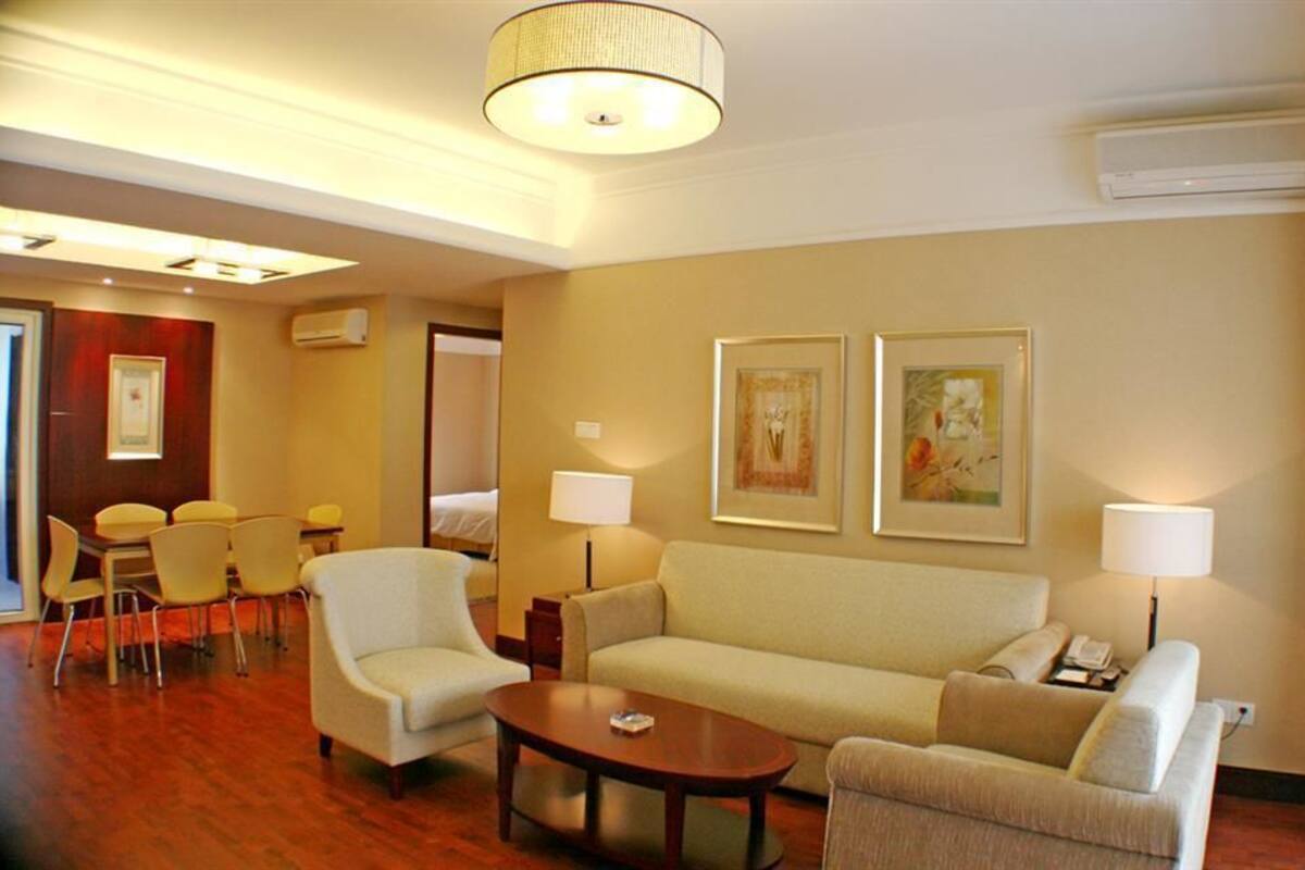 A hotel room with a sofa, armchairs, a coffee table, and a dining area with chairs and a table.