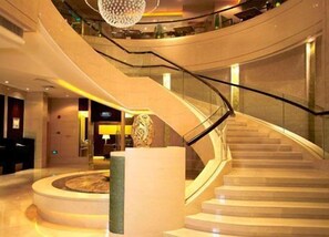A modern hotel lobby with a curved staircase, a reception desk, and a decorative sculpture.