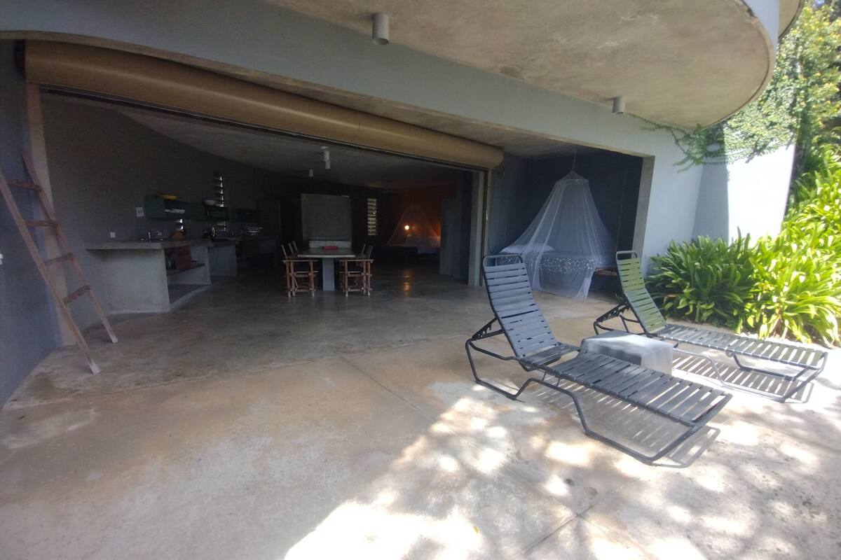 A covered patio area with two lounge chairs, a table, and a kitchen visible through an open door.