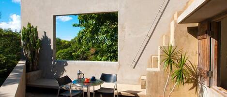 An outdoor seating area with a table and chairs, a potted plant, and a view of greenery.