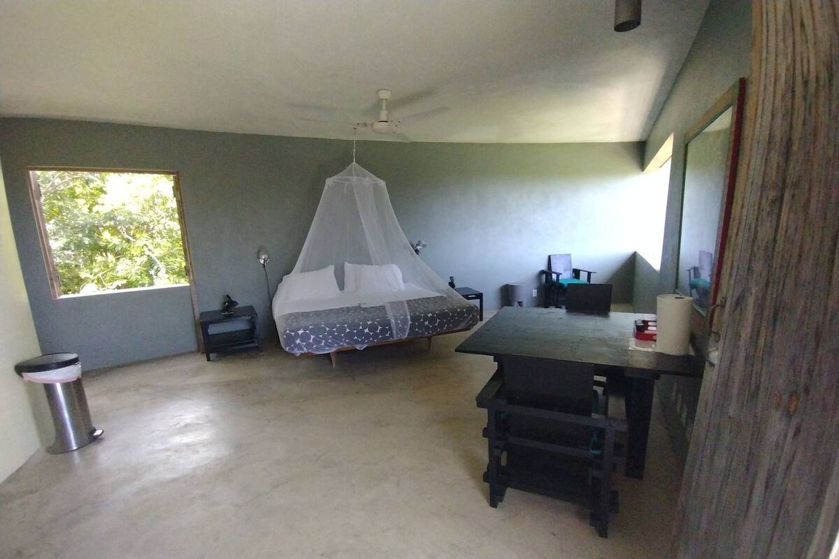 A room with a bed, a desk, a chair, a trash bin, and a ceiling fan.