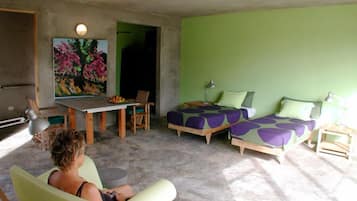A room with a green wall, a dining table with chairs, a bed with purple bedding, and a ceiling fan.