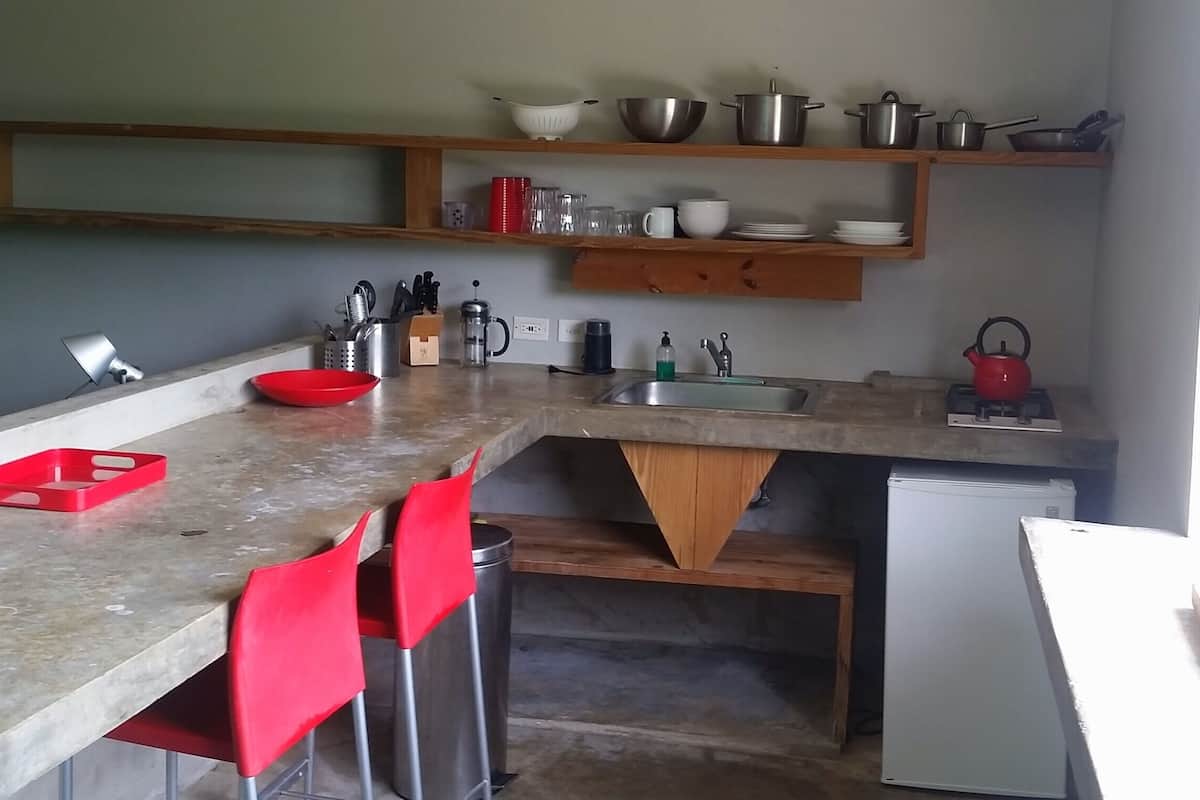 A kitchen with a granite countertop, red chairs, a sink, a stove, and various kitchen utensils.