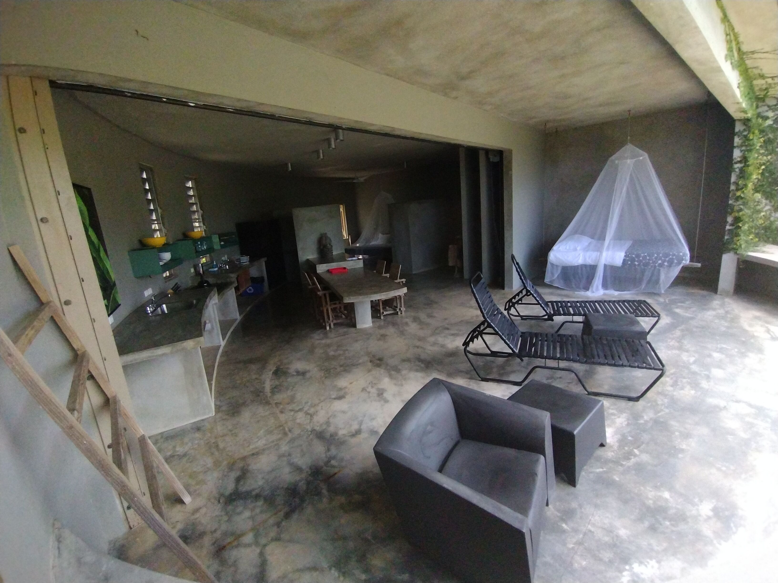 Un garaje abierto con piso de concreto, una mesa de comedor con sillas y una zona de estar cubierta con toldo.
