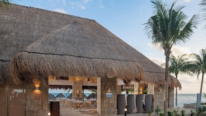 Un resort con una edificación de techo de paja, zona de comedor al aire libre y vistas al océano.