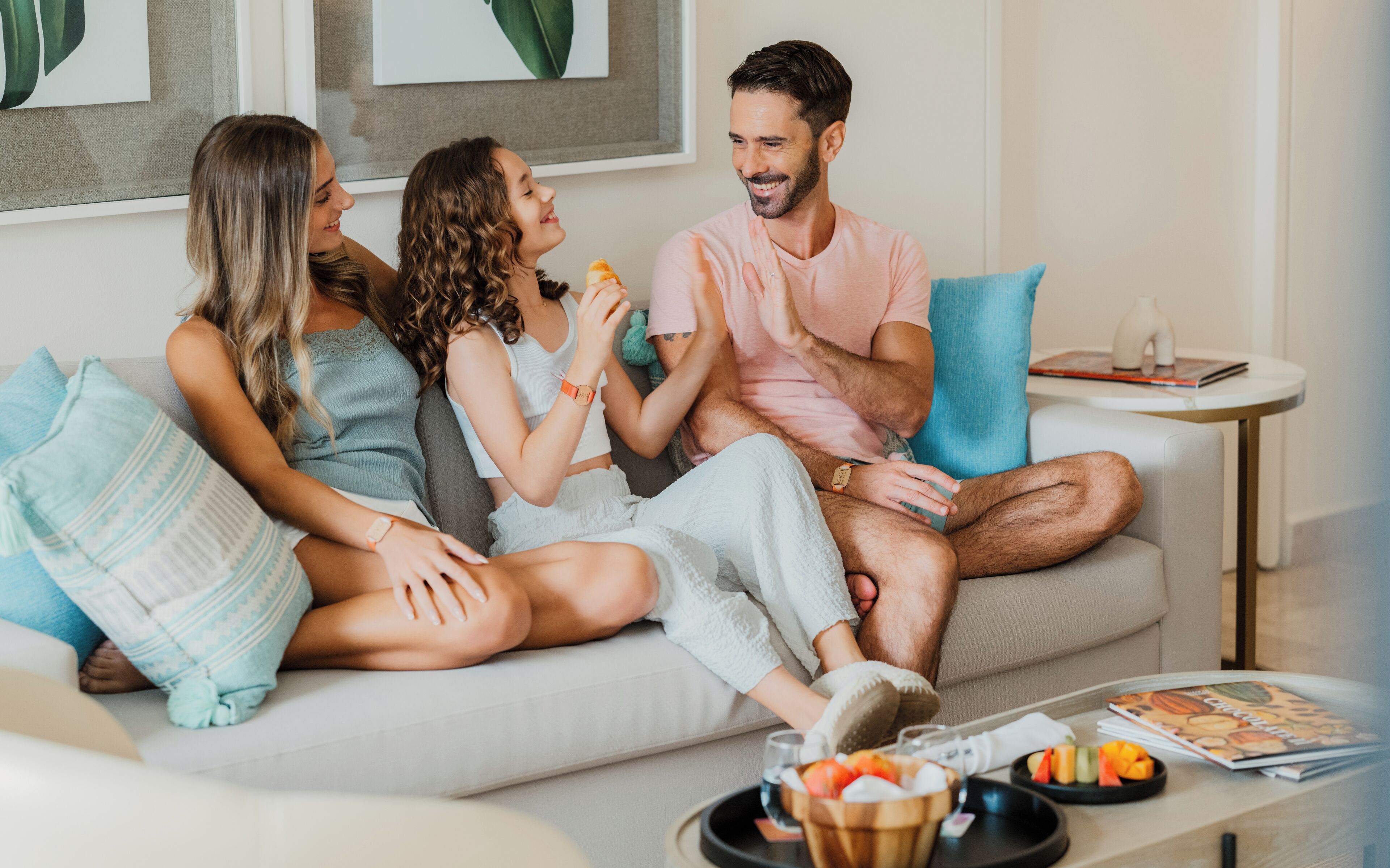 Ein modernes Wohnzimmer mit einer Couch, Kissen, einem Couchtisch mit Früchten und einer Zeitschrift sowie einem kleinen Beistelltisch mit einer Vase.