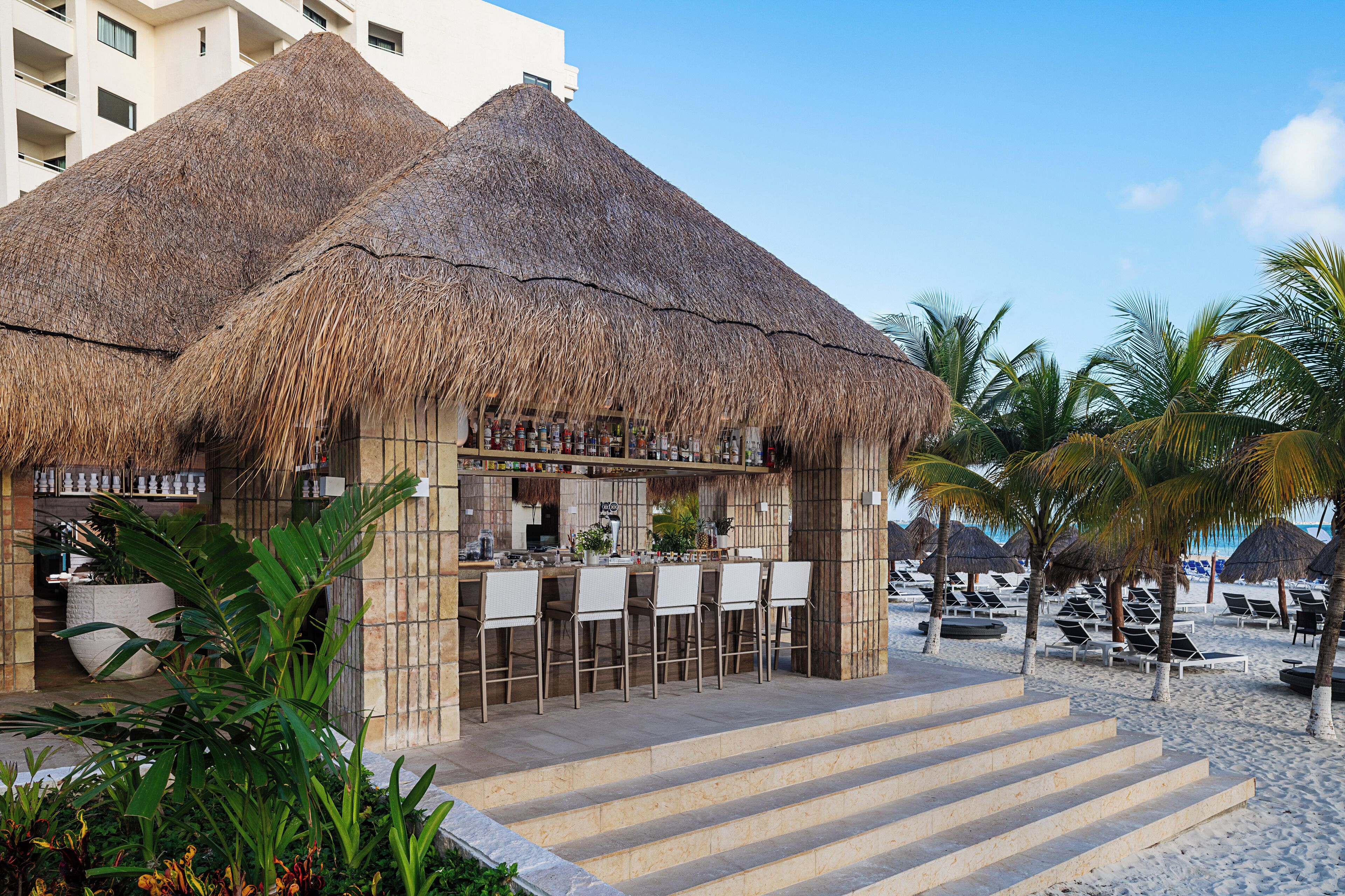 A beachside bar with thatched roofs, outdoor seating, and palm trees.