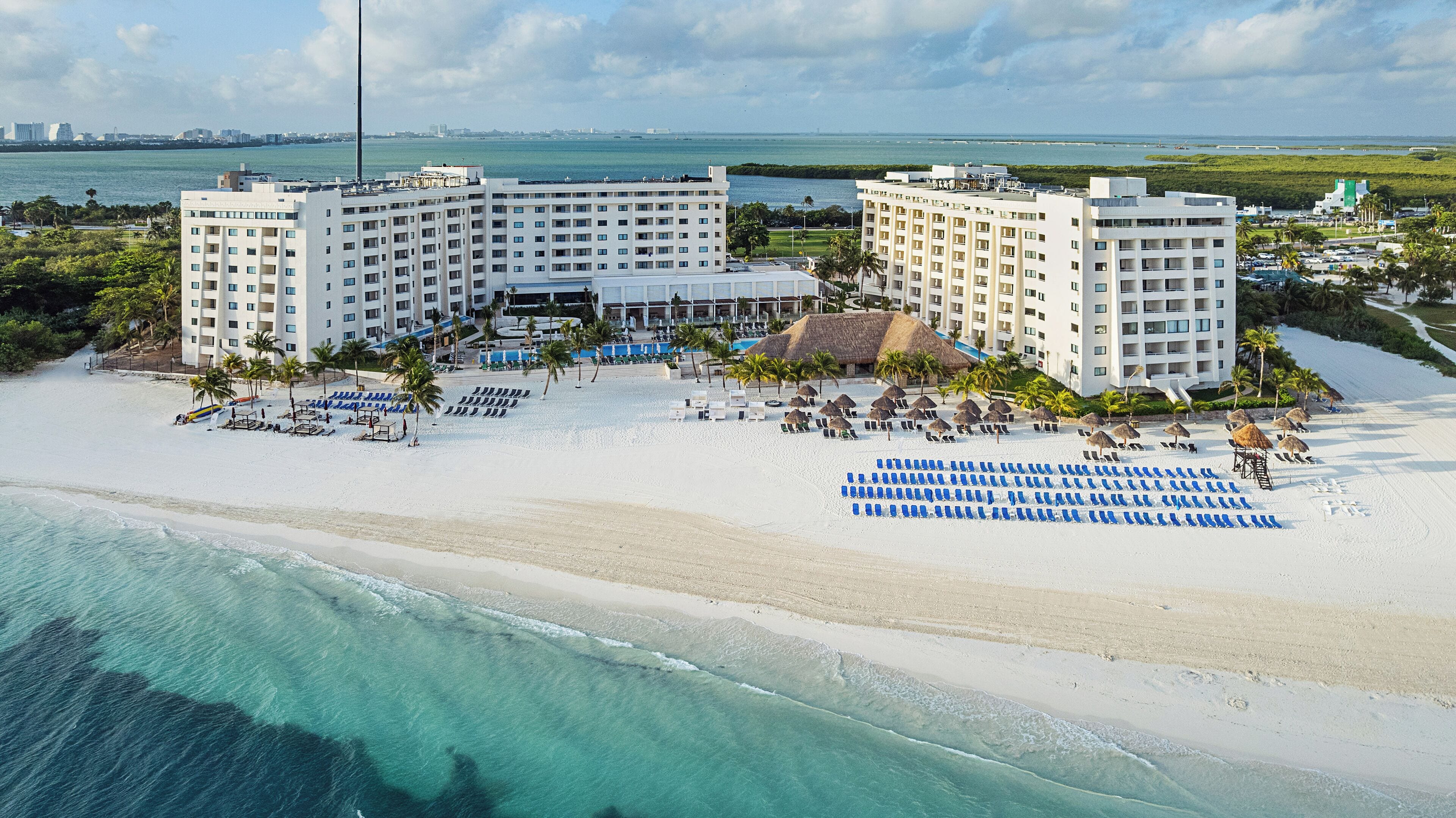 Un resort con varias edificaciones, una playa con tumbonas y vista al océano.