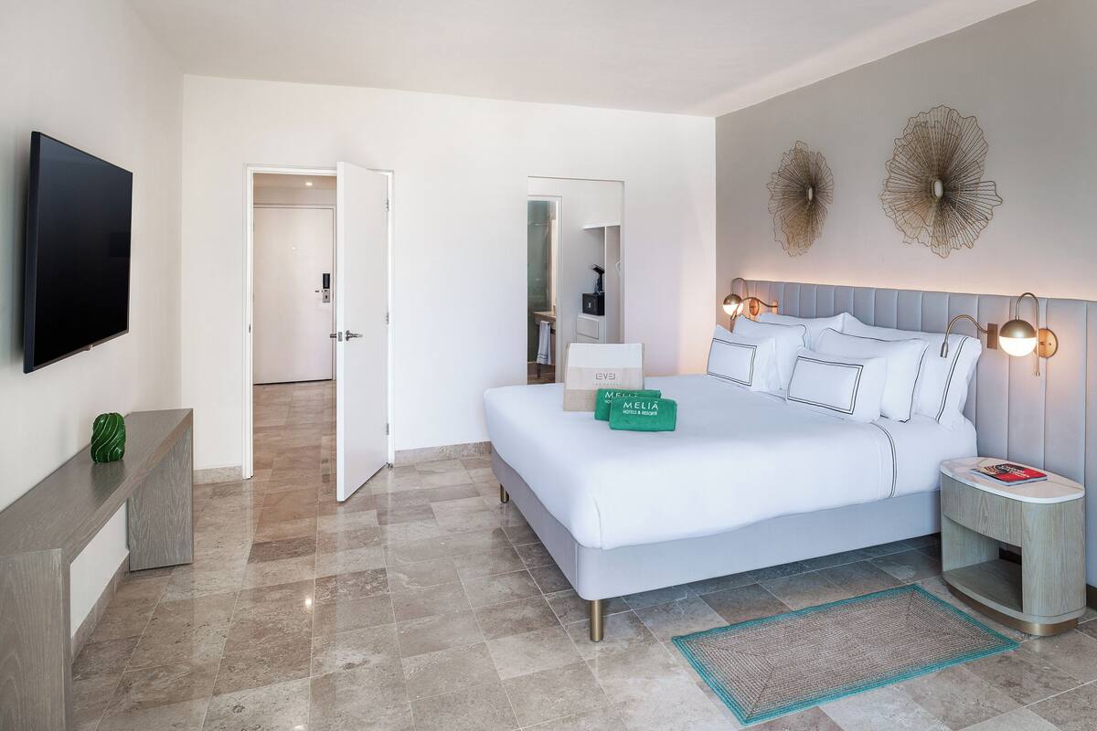 A modern hotel room with a large bed, a bedside table, a TV, and a mirror.