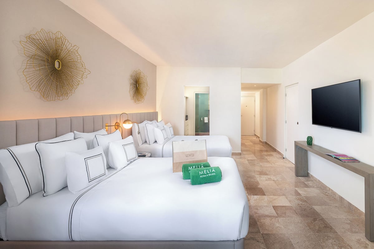 A hotel room with a bed, a TV, a desk, and a hallway leading to another room.