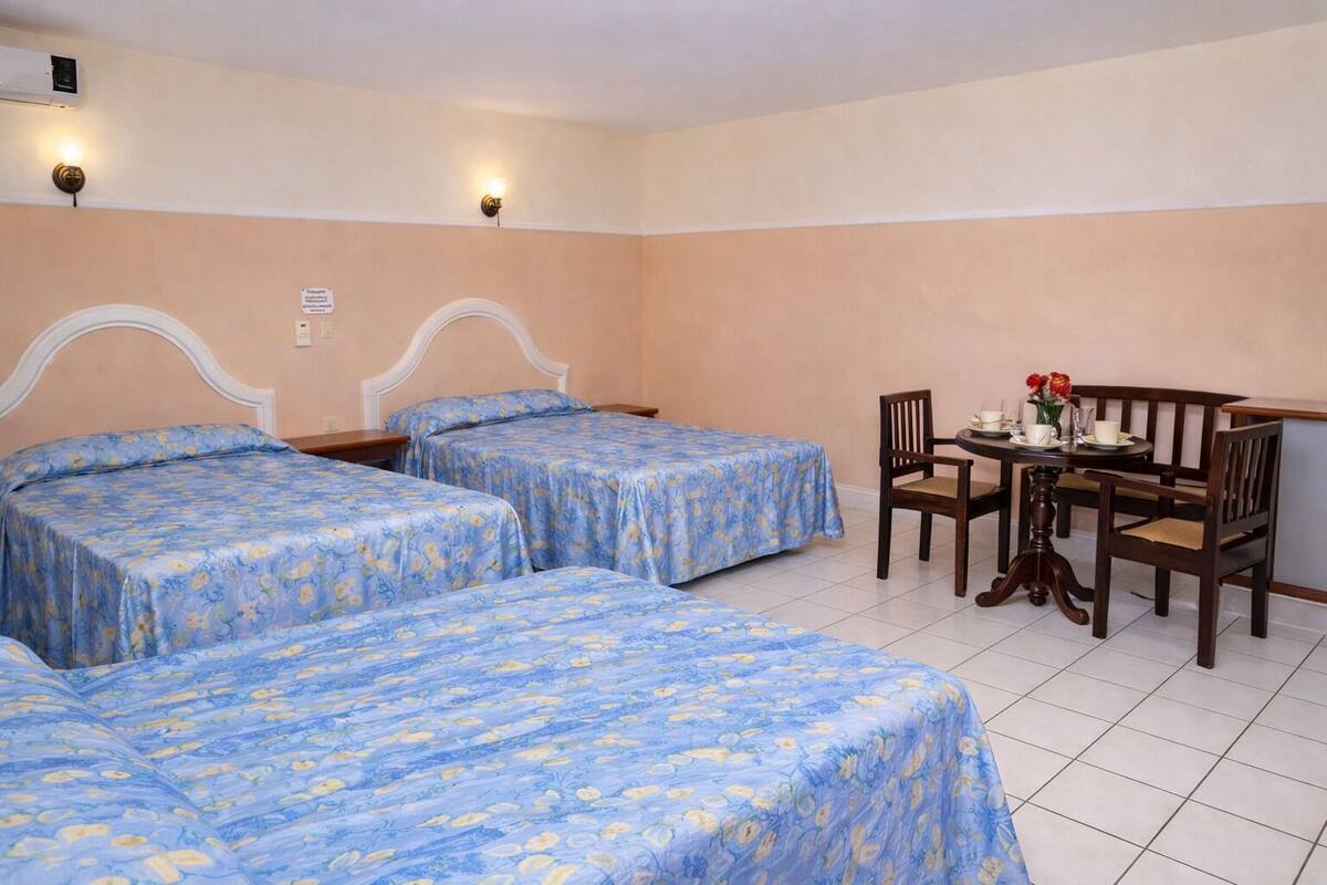 A hotel room with two beds, a small table with chairs, and a wall-mounted air conditioner.