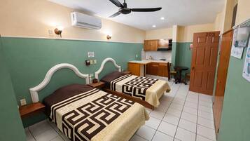 A hotel room with two beds, a desk, a chair, a ceiling fan, an air conditioning unit, and a door with the number 203.
