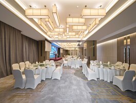 Un amplio salón de banquetes con candelabros escalonados, mesas cubiertas de blanco y sillas dispuestas para un evento formal.