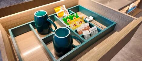 Un cassetto suddiviso in scomparti con una tazza blu, una tazza verde e pacchetti di tè Lipton.