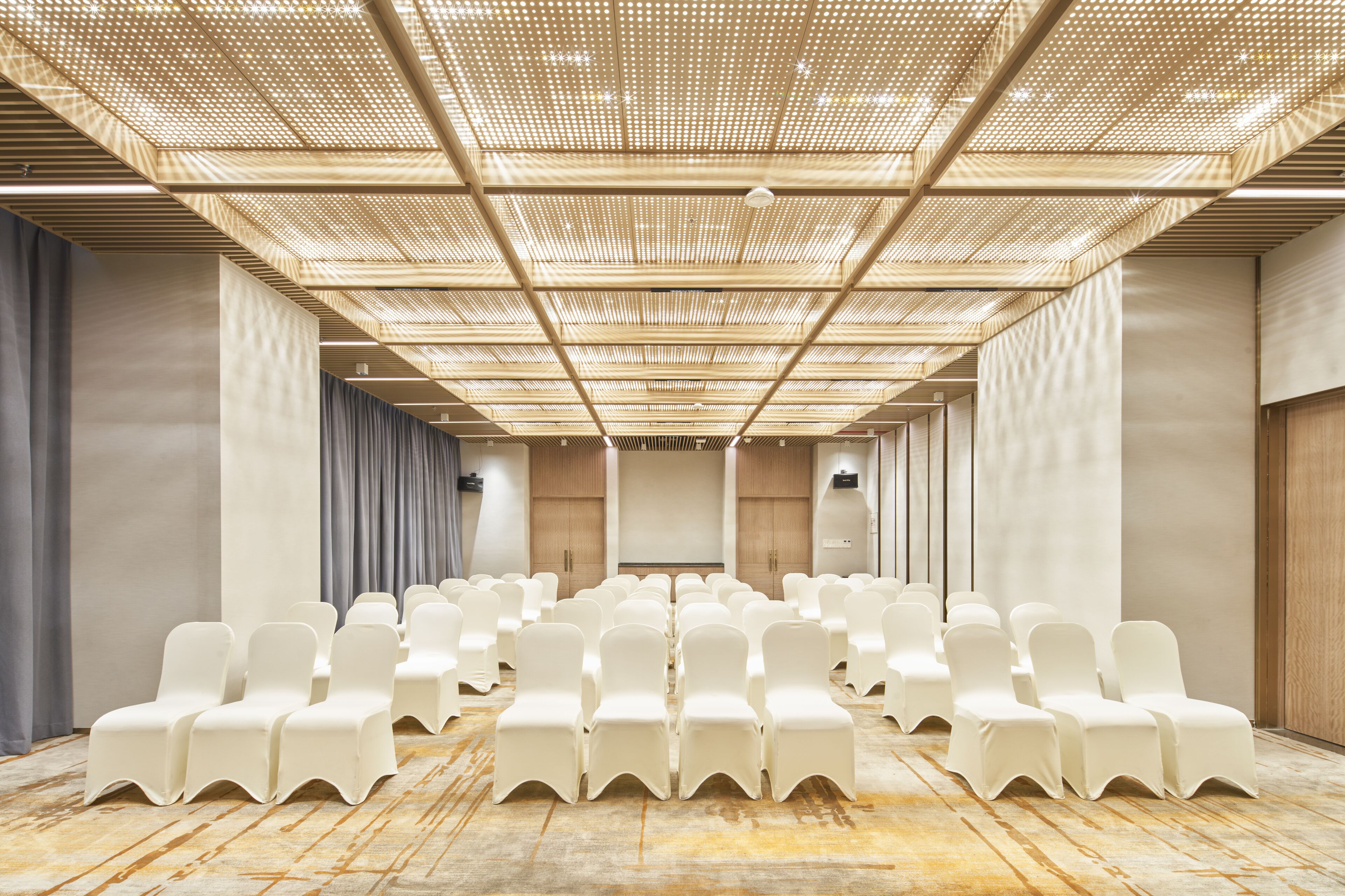 A conference room with rows of white chairs, a wooden floor, and a ceiling with a grid pattern.