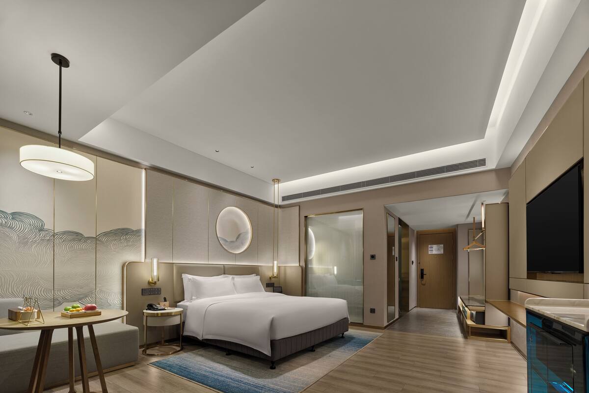Une chambre d’hôtel moderne, dotée d’un grand lit, de tables de chevet, d’un bureau et d’une télévision.