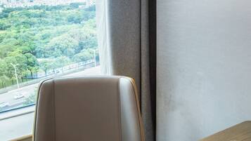 A room with a view of a cityscape, a window, a table with a book and a glass of water.