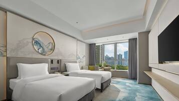 A modern hotel room with two beds, a large window with a city view, a flat-screen TV, and a small table with a vase.
