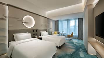 A hotel room with two beds, a round mirror, a desk, a chair, and a large TV.