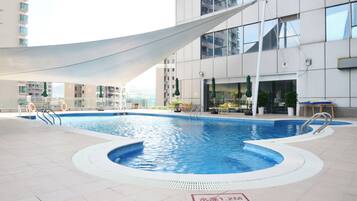 An indoor swimming pool with a white shade sail, surrounded by a modern building with balconies and outdoor seating.