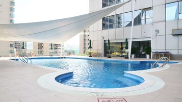 An indoor swimming pool with a white shade sail, surrounded by a modern building with balconies and outdoor seating.