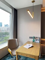 Habitación de hotel con una mesa de madera, una silla, una ventana con vistas a la ciudad, una lámpara colgante y una planta pequeña sobre la mesa.