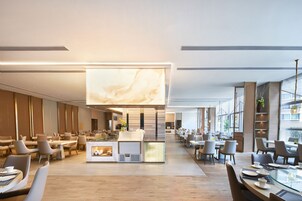 A modern hotel lobby with a central bar area, seating arrangements, and large windows providing natural light.