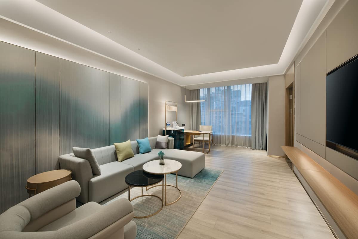 Une chambre d’hôtel moderne comprenant un canapé, une table basse ronde, un téléviseur et un bureau avec une chaise.