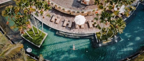 Vista aérea de un resort con piscina circular, áreas de descanso y palmeras.