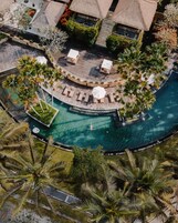 Vista aérea de un resort con piscina circular, áreas de descanso y palmeras.
