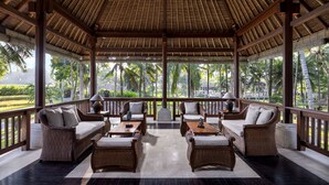 A covered outdoor seating area with wicker furniture and a view of palm trees. - The Ubud Village Resort & Spa (Ubud)
