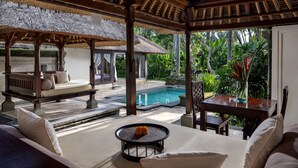 A covered outdoor seating area with a pool, wooden furniture, and tropical plants. - The Ubud Village Resort & Spa (Ubud)