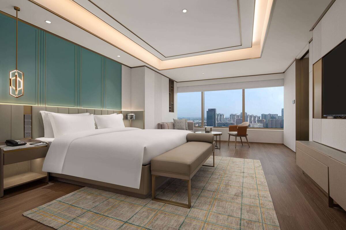 A modern hotel room with a large bed, a bench, a desk, and a TV.