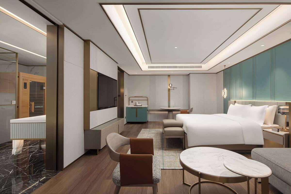 A modern hotel room with a large bed, a desk, a sofa, and a TV.