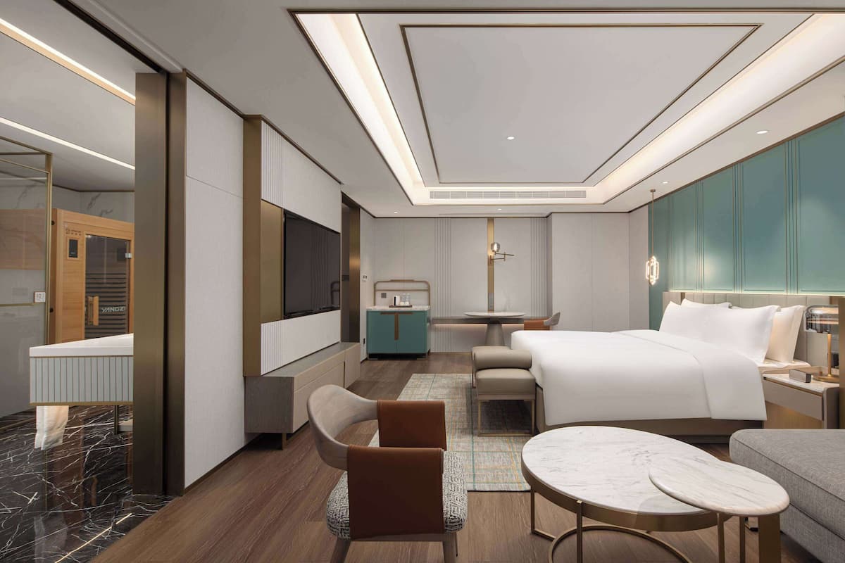 A modern hotel room with a large bed, a desk, a sofa, and a TV.