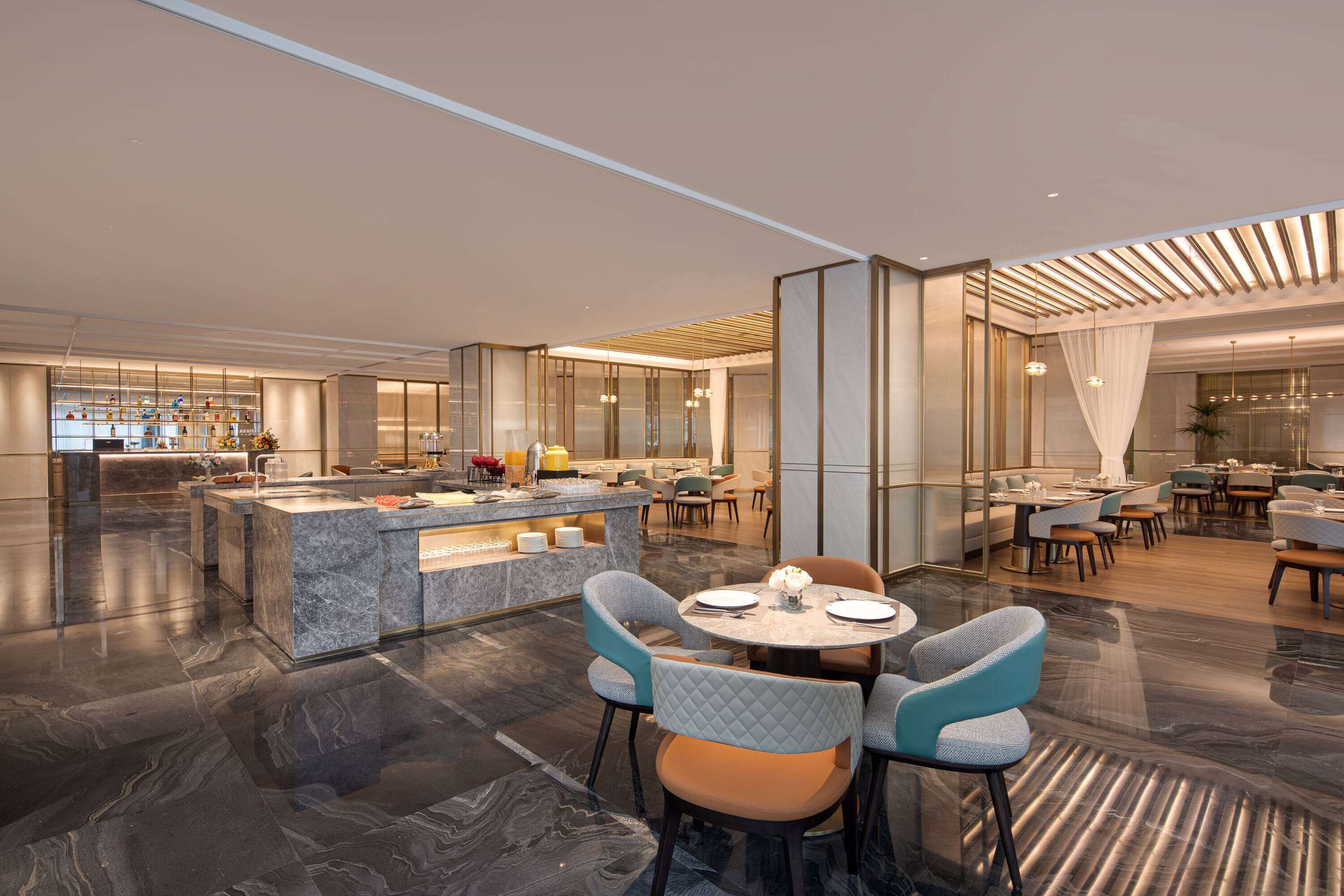 Un hall d’hôtel moderne avec un comptoir d’accueil en marbre, des tables rondes et des coins salons confortables.
