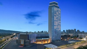 A modern hotel with a prominent glass facade, a parking lot, and a cityscape in the background. - Wyndham Hangzhou Linping (Hangzhou)
