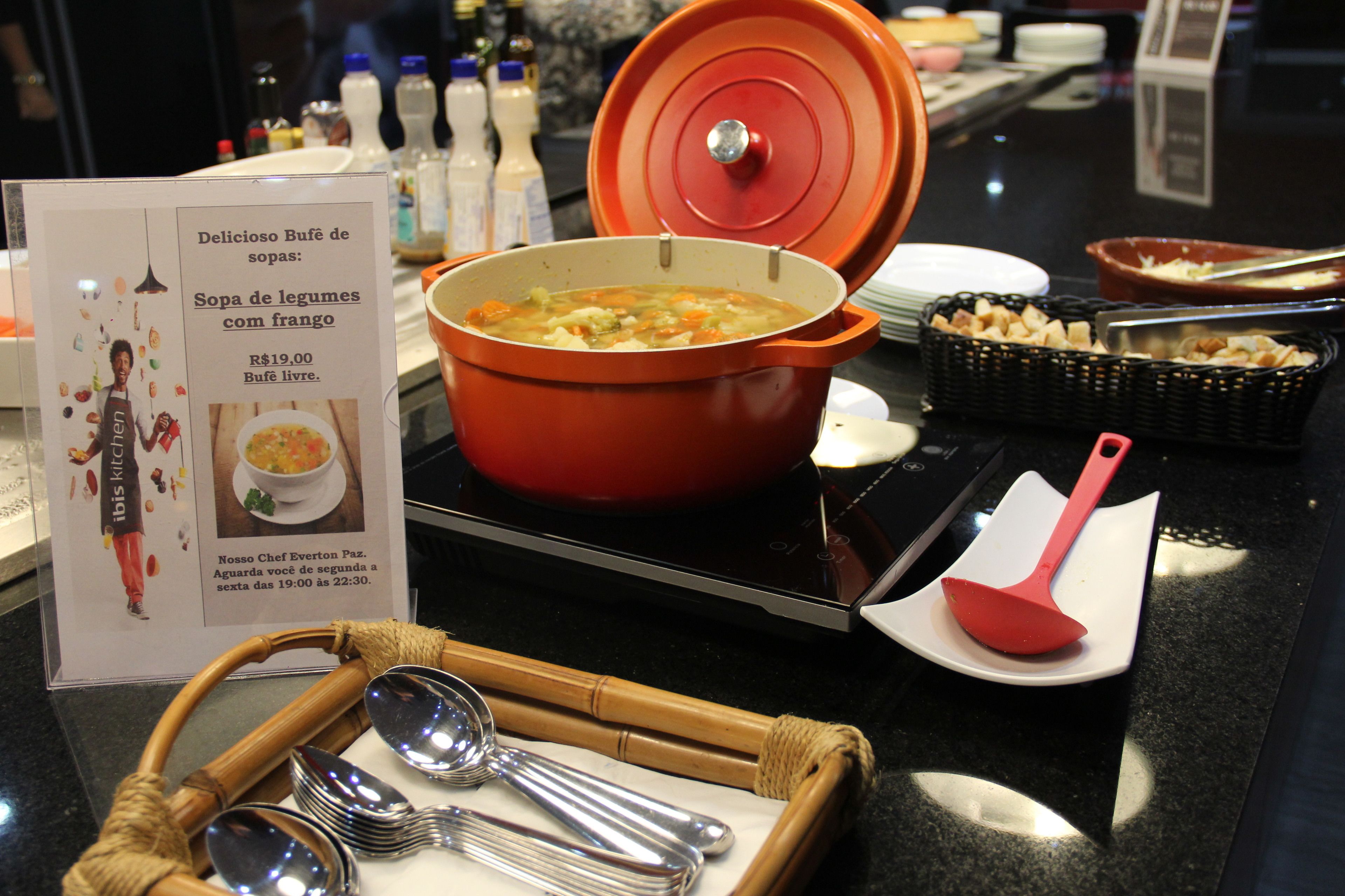 En buffetopsætning med en stor gryde suppe, serveringsbestik og et skilt, der beskriver menuen.
