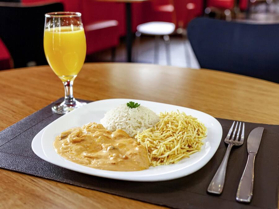 Un plato de arroz, un guiso cremoso y papas fritas sobre una mesa con un vaso de jugo de naranja.