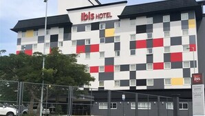 A modern hotel building with a checkered facade, a prominent 'ibis HOTEL' sign, and a fenced parking area. - ibis Criciúma (Criciuma)