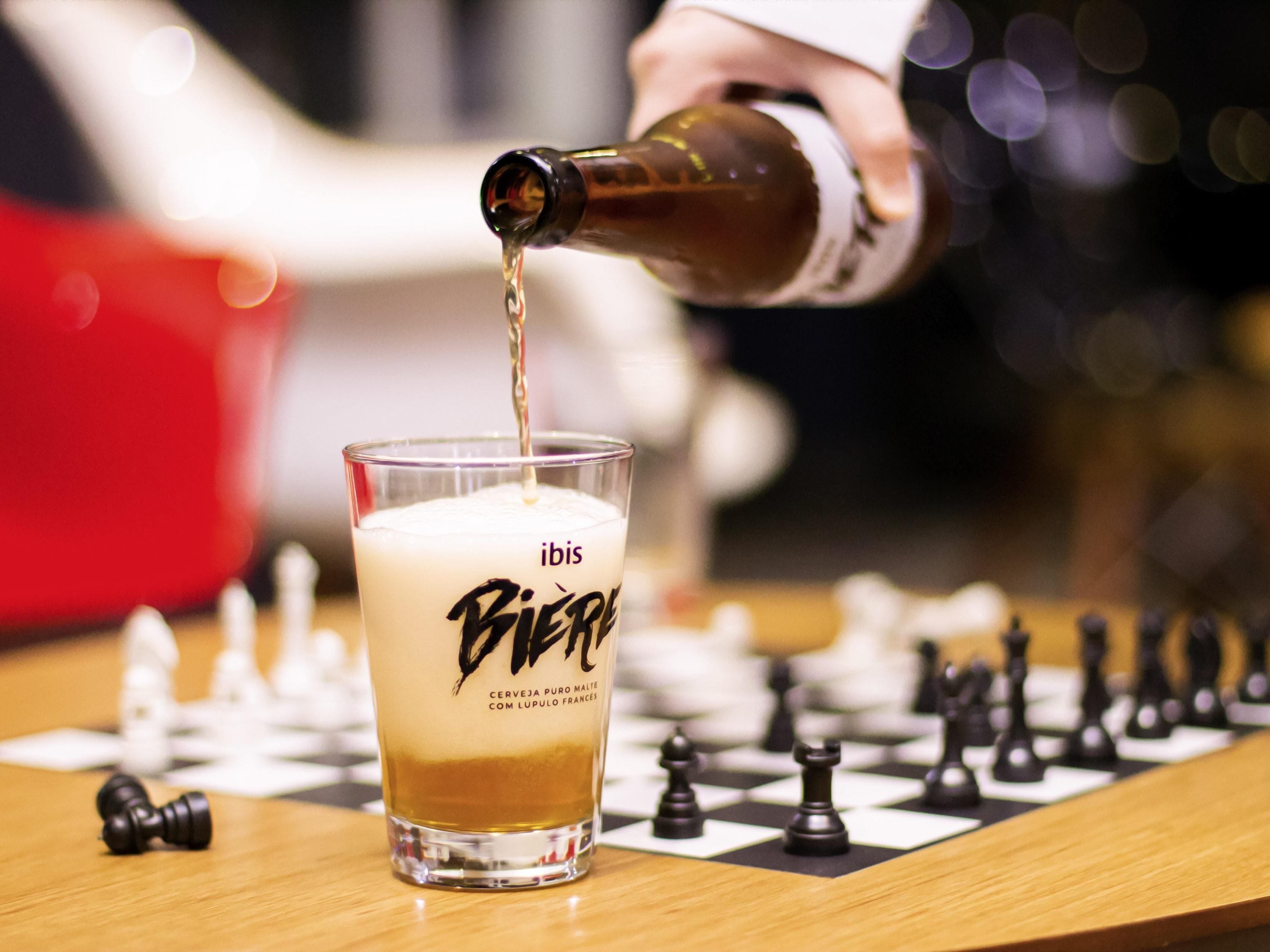 A glass of beer with a label, a chessboard, and chess pieces.