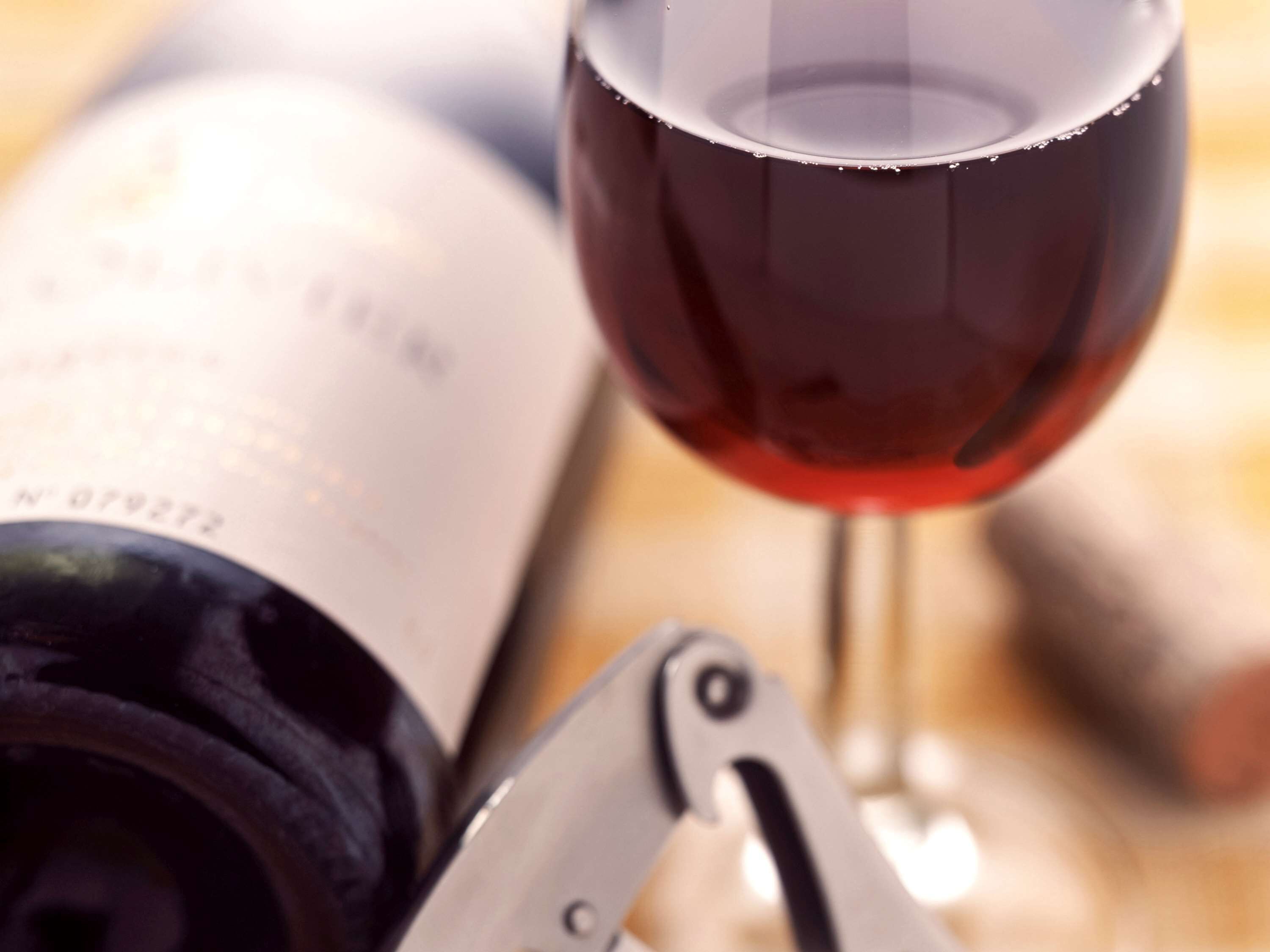 A wine bottle and a wine glass with a corkscrew.