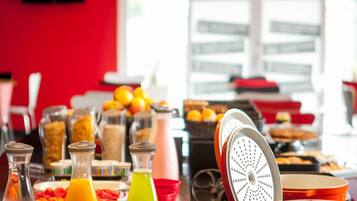 Buffet de café da manhã com diversas opções de comida e bebidas, incluindo suco de laranja e um smoothie verde.