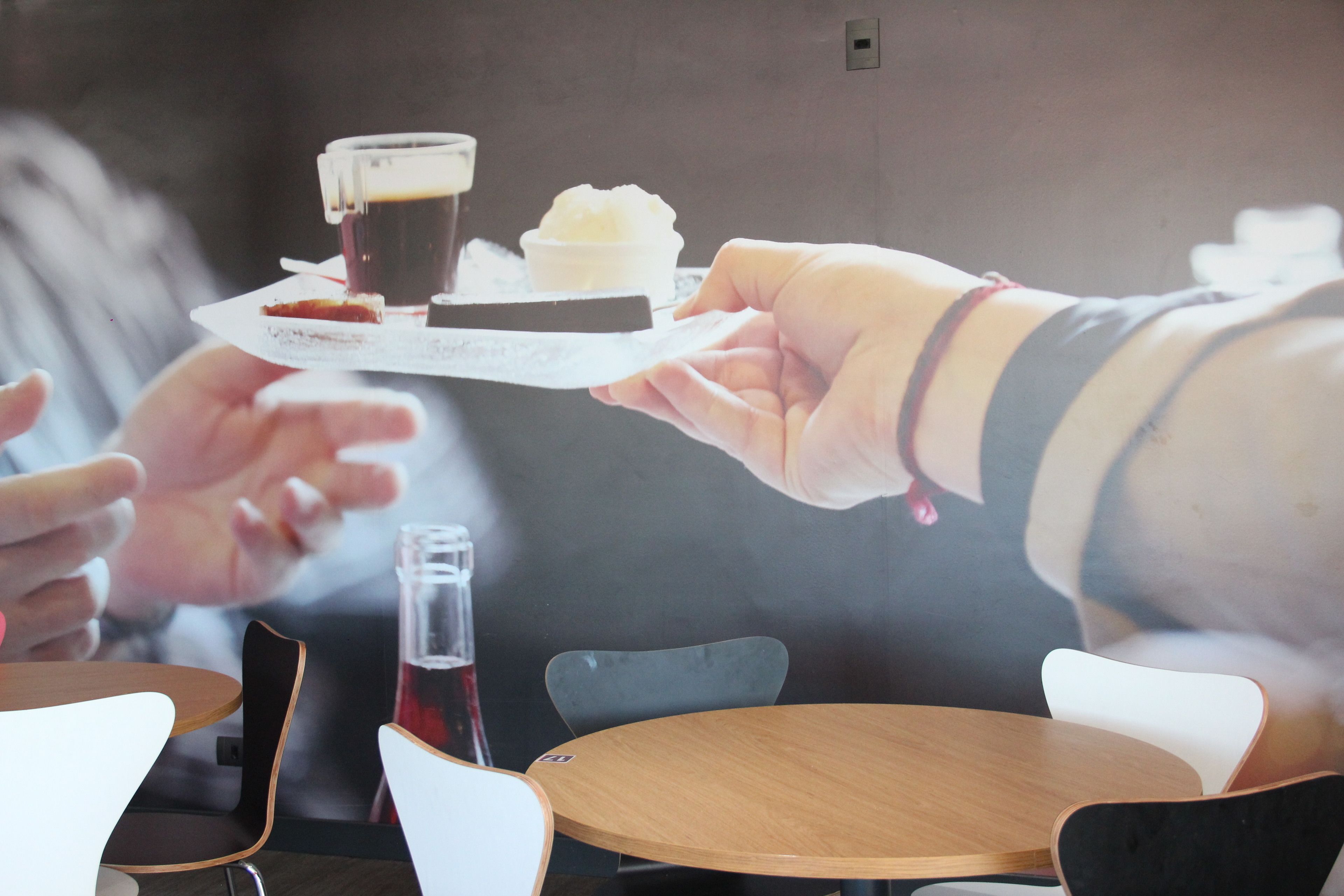 Una persona sostiene una bandeja con una porción de pastel y una taza de café.