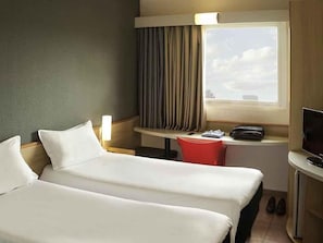 A hotel room with two beds, a desk with a chair, a television, and a window with curtains. - ibis Criciúma (Criciuma)