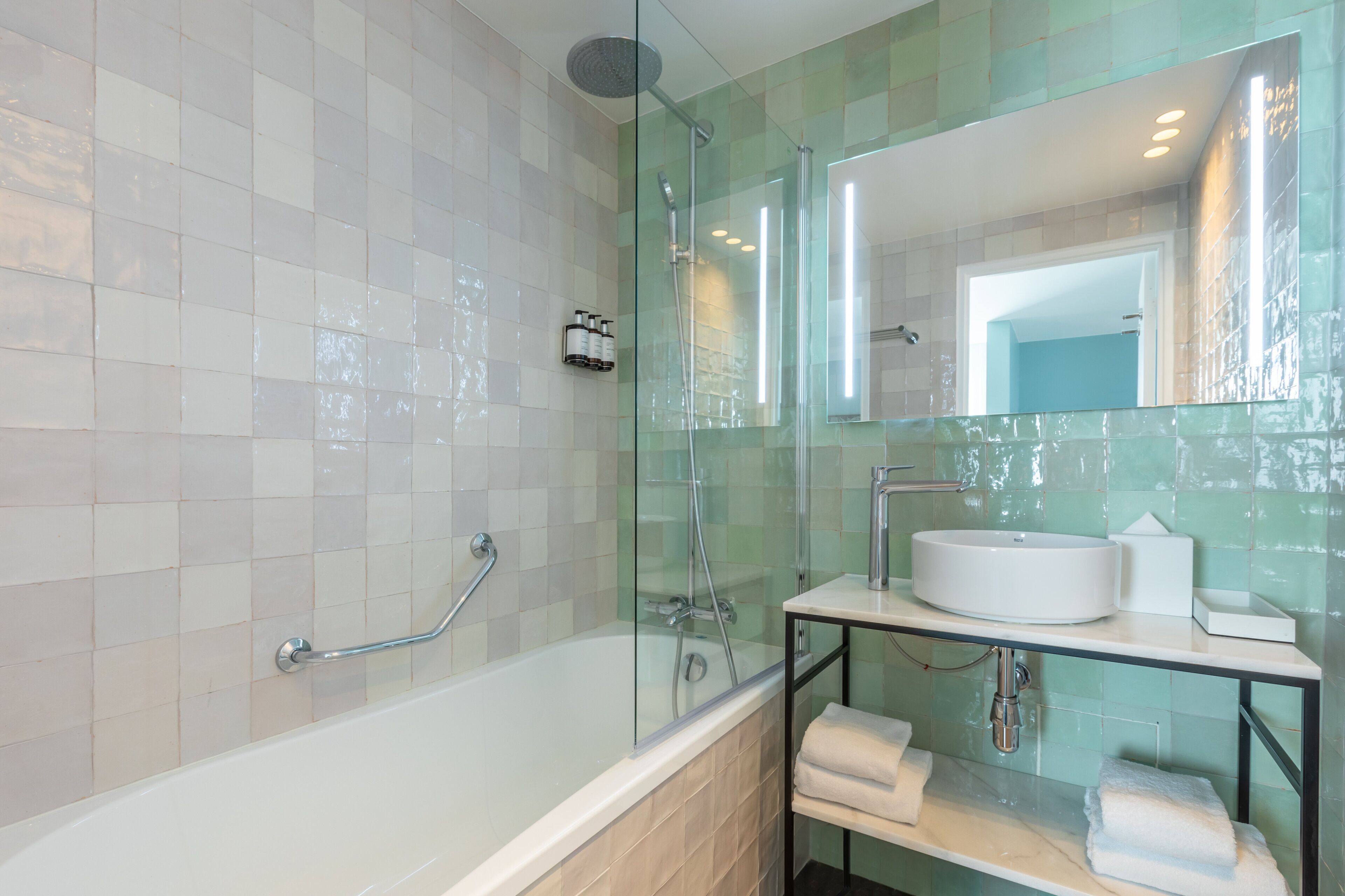 A modern bathroom with a glass-enclosed shower, a white bathtub, and a vanity with a sink and towel rack.